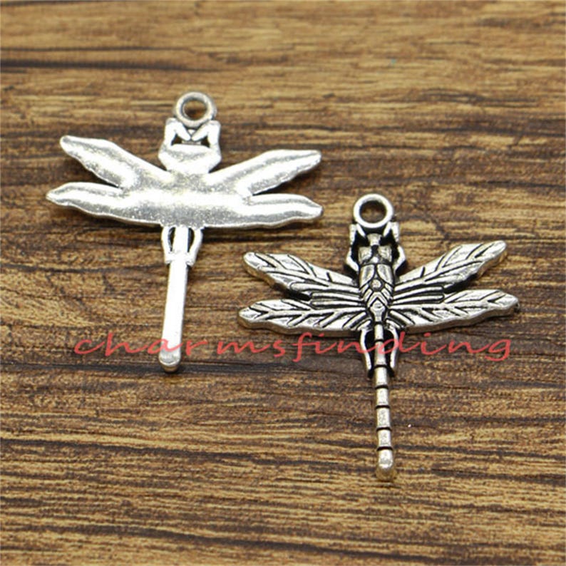 May include: Two silver dragonfly charms with intricate details. The charms have a loop at the top for attaching to jewelry or other crafts.