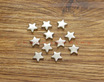 May include: A group of 12 silver star-shaped metal charms. The charms are scattered on a wooden surface.