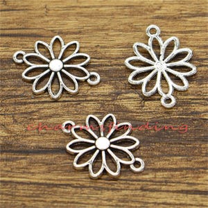 May include: Three silver-toned metal charms in the shape of a daisy flower. Each charm has a loop for attaching to jewelry or other crafts.