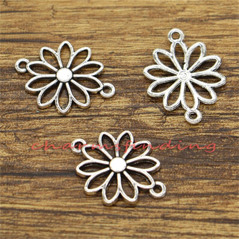 May include: Three silver-toned metal charms in the shape of a daisy flower. Each charm has a loop for attaching to jewelry or other crafts.