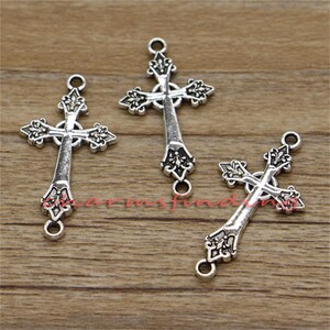 May include: Three silver-toned metal cross charms with ornate details. Each cross has a loop at the top and bottom for attaching to jewellery or other crafts.