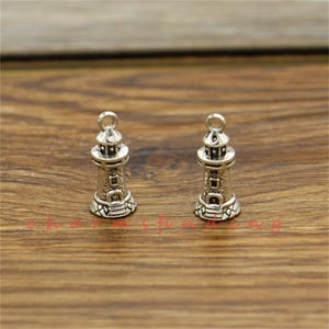 Puede incluir: Dos encantos de faro plateados con detalles intrincados. Los encantos son pequeños y tienen un bucle en la parte superior para sujetarlos a joyas u otras manualidades.