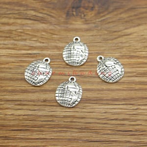 May include: Four small, silver-coloured globe charms with a loop at the top for jewellery making. Each charm features a detailed representation of the Earth, with grid lines and continents visible. The charms are displayed on a wooden surface.