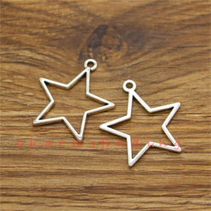 May include: Two silver-toned metal star-shaped charms with a loop at the top for attaching to jewelry or other crafts.