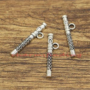 Puede incluir: Tres abalorios de metal plateados en forma de flautas con detalles decorativos. Cada abalorio tiene un pequeño bucle en la parte superior para sujetarlo a joyas u otras manualidades.