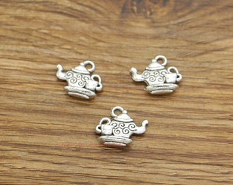 May include: Three silver charm pendants shaped like teapots with a cup on the side. The teapots have a detailed design with swirls and a handle.