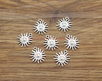 May include: Eight silver sun charm pendants with a raised circle in the center. The charms are on a wooden surface.