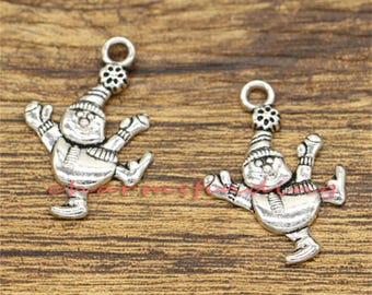 May include: Two silver charm pendants in the shape of a snowman wearing a hat and scarf. The snowman is in a skating pose with one leg raised and one arm outstretched.