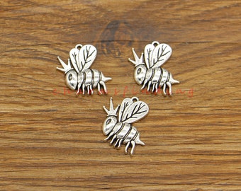 Puede incluir: Tres abalorios de abeja plateados con una corona en la cabeza y alas. Las abejas están detalladas con rayas y tienen un bucle en la parte superior para sujetarlas a joyas.