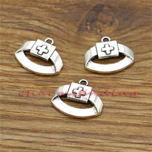 May include: Three silver-toned metal charms shaped like a first aid kit with a white cross in the center. The charms are perfect for adding a unique touch to jewelry or crafts.