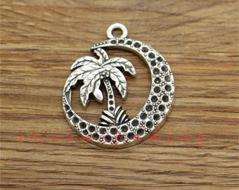 May include: Silver charm pendant featuring a palm tree inside a crescent moon design. The charm has a textured surface and is perfect for jewelry making.