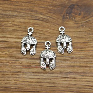 May include: Three silver-toned metal charms shaped like Roman helmets. Each charm has a loop at the top for attaching to a necklace or bracelet.
