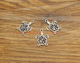 May include: Three silver turtle charms with an intricate filigree design. The turtles are on a wooden surface.