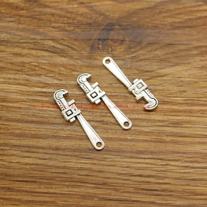 Op de afbeelding: Drie zilverkleurige verstelbare moersleutelbedels. De bedels zijn ongeveer 5 cm lang en hebben een gedetailleerd ontwerp.