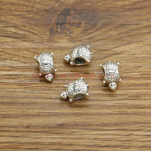 Puede incluir: Cuatro cuentas de amuleto de tortuga plateadas con un agujero en el centro para enhebrar en una pulsera o collar.