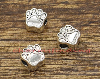 May include: Three silver charm beads in the shape of a paw print. The beads are detailed and have a slightly aged look.