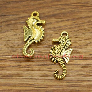 May include: Two gold-toned seahorse charms. The seahorses are detailed with textured scales and have a slightly aged look.