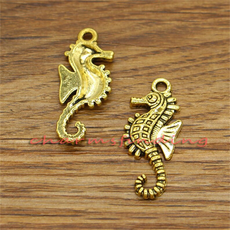 May include: Two gold-toned seahorse charms. The seahorses are detailed with textured scales and have a slightly aged look.