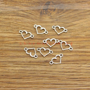 May include: Silver heart-shaped connector charms with two jump rings on each charm. The charms are scattered on a wooden surface.