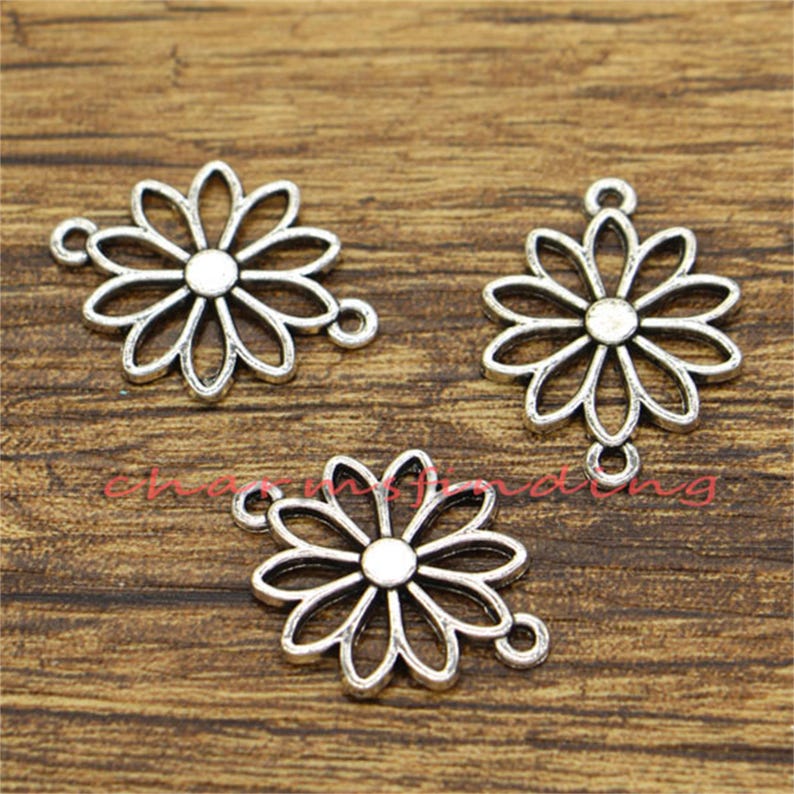 May include: Three silver-toned metal charms in the shape of a flower with a hole in the center. The charms have a vintage look and are perfect for jewelry making.