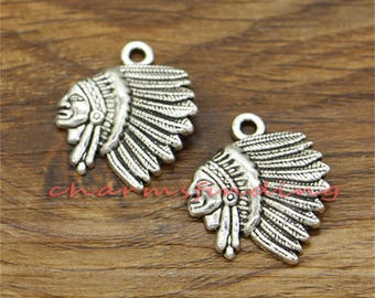 May include: Two silver-toned metal charms in the shape of Native American headdresses. Each charm features a detailed profile of a person wearing a headdress with feathers.