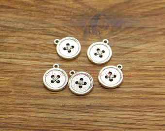 May include: Five silver-toned metal button charms with a cross-stitch design. The charms are round and have a hole at the top for attaching to jewelry or other crafts.