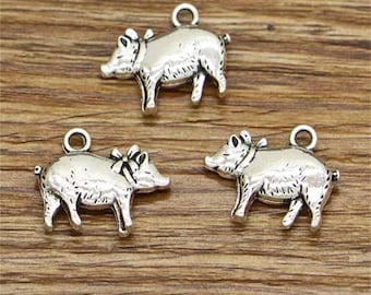 May include: Three silver pig charms with a bow on their head. The charms are perfect for adding a touch of whimsy to jewelry or crafts.