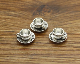 May include: Three miniature silver teacups and saucers with ornate designs. The cups and saucers are made of metal and have a silver finish.