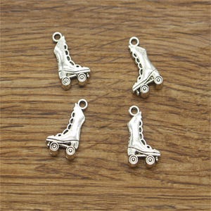 Puede incluir: Cuatro abalorios de patines de ruedas plateados con un diseño detallado. Cada abalorio presenta una bota con ruedas y un bucle para sujetarlo a un collar o pulsera.