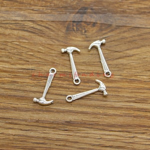 May include: Five silver-toned hammer charms with a loop for attaching to jewellery or crafts.