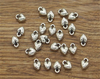 May include: A collection of silver-toned heart-shaped charms with a loop at the top. The charms are scattered on a wooden surface.