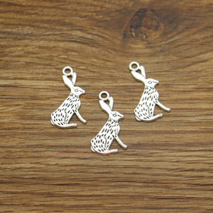 May include: Three silver-coloured rabbit charms with a textured design. Each charm features a sitting rabbit with long ears and a small loop at the top for attaching to jewellery or other crafts. The charms are displayed on a wooden surface.