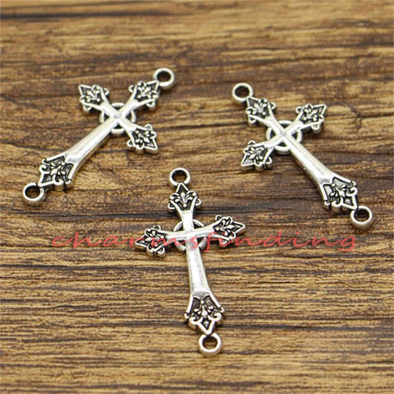 May include: Three silver-toned cross charms with ornate details. Each charm has two jump rings for attaching to jewellery or other crafts.