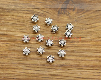 May include: A collection of silver-toned metal flower-shaped beads. The beads are scattered on a wooden surface.