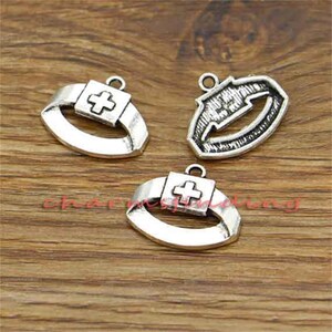 May include: Three silver-toned metal charms with a cross design. The charms are in the shape of a medical symbol, a cross, and a stylized medical symbol.