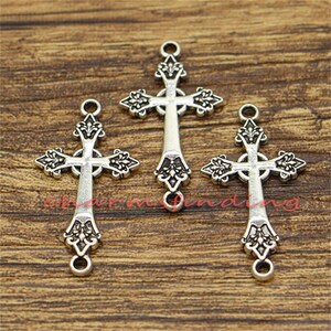 May include: Three silver-toned cross charms with ornate details. Each cross has a loop at the top and bottom for attaching to jewellery or other crafts.