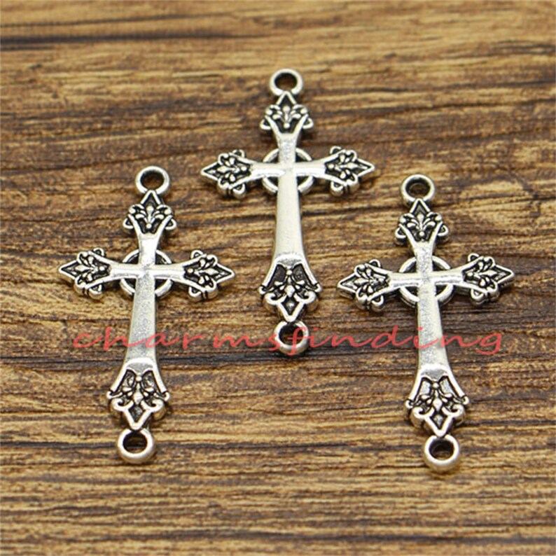 May include: Three silver-toned cross charms with ornate details. Each cross has a loop at the top and bottom for attaching to jewellery or other crafts.