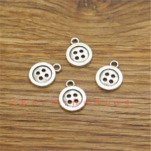 Könnte beinhalten: Vier silberne Anhänger in Form von Knöpfen mit jeweils vier Löchern. Die Knöpfe liegen auf einer Holzoberfläche.
