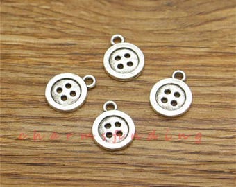 May include: Four silver charm pendants shaped like buttons with four holes each. The buttons are on a wooden surface.