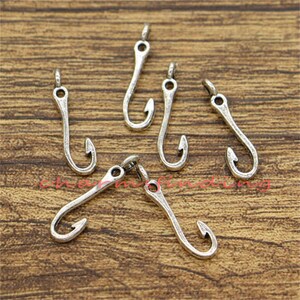 May include: Six silver-toned metal fishing hook charms. The hooks are all the same size and shape, with a small loop at the top for attaching to jewelry or other crafts.