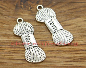 May include: Two silver-toned metal charms shaped like spools of yarn. Each charm has the word "Yarn" engraved on it.