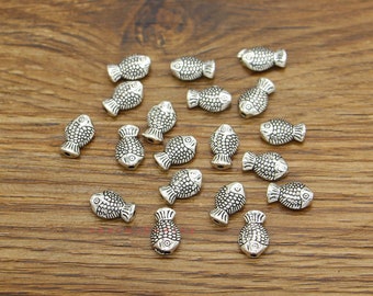 May include: A collection of silver-toned fish-shaped beads. The beads are small and have a detailed design. They are perfect for jewelry making or other craft projects.