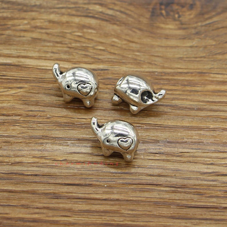 May include: Three silver charm beads in the shape of elephants with a small heart on each elephant's trunk.