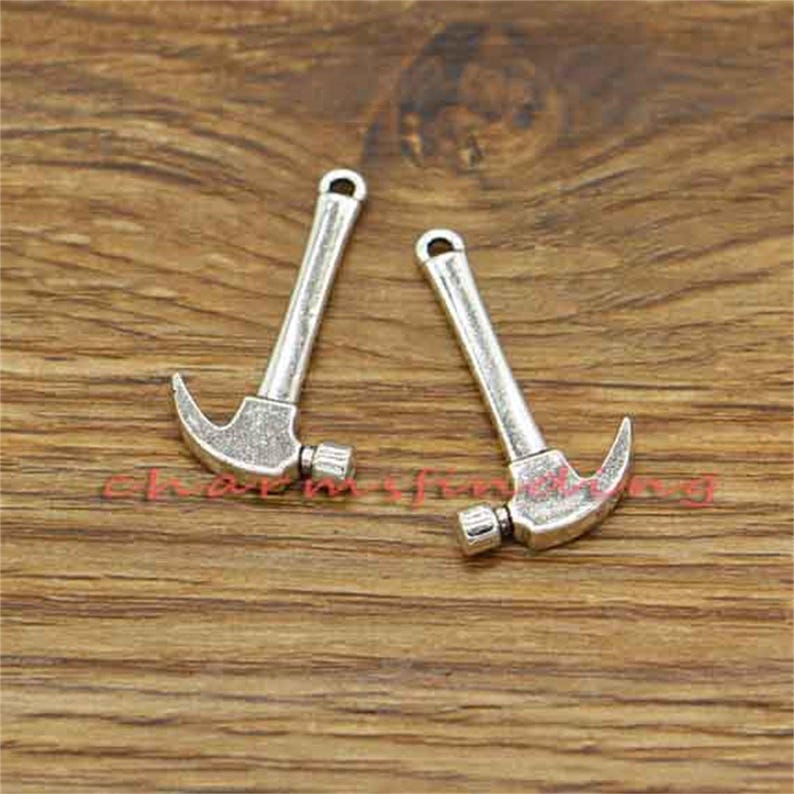 May include: Two silver-toned hammer charms with a loop at the top for attaching to jewelry or other crafts.