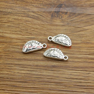 May include: Three silver charm pendants shaped like empanadas. The charms have a textured surface and a loop for attaching to a chain or bracelet.