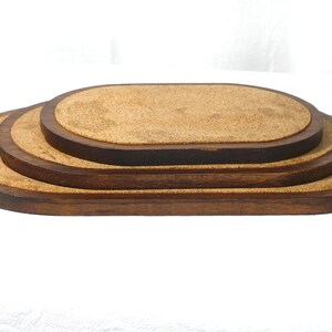 May include: A set of three nested oval-shaped trays featuring dark brown wooden frames and light brown cork inserts. The trays are stacked on top of each other, with the largest base tray at the bottom and the smallest tray at the top.