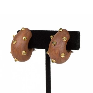 May include: A pair of brown wooden hoop earrings with gold accents. The earrings are displayed on a black stand.