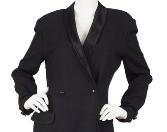 May include: A black double-breasted dress with a satin lapel collar. The dress features two front pockets and is displayed on a mannequin. The sleeves have buttoned cuffs. The dress is knee-length.