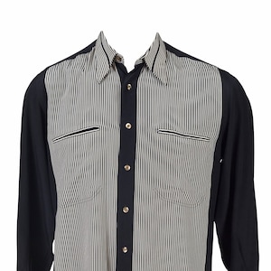 May include: A black and white striped long-sleeve shirt with a button-up front and two pockets. The shirt has a contrasting black panel down the center.