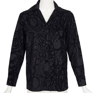 May include: A long-sleeved black button-down shirt featuring a tonal, abstract circular and grid-like pattern throughout the fabric. The shirt has a classic collar, a front button placket with matching black buttons, and cuffs at the wrists.
